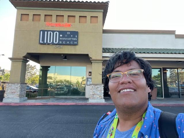 Smiling person posing outside a restaurant with a LIDO Manhattan Beach sign